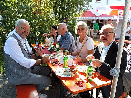 Mehrere Menschen sitzen an einem Biertisch und esssen.