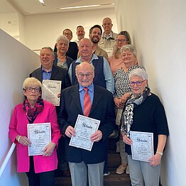 Gruppenfoto mit Menschen auf einer Treppe, die Urkunden in den Händen halten