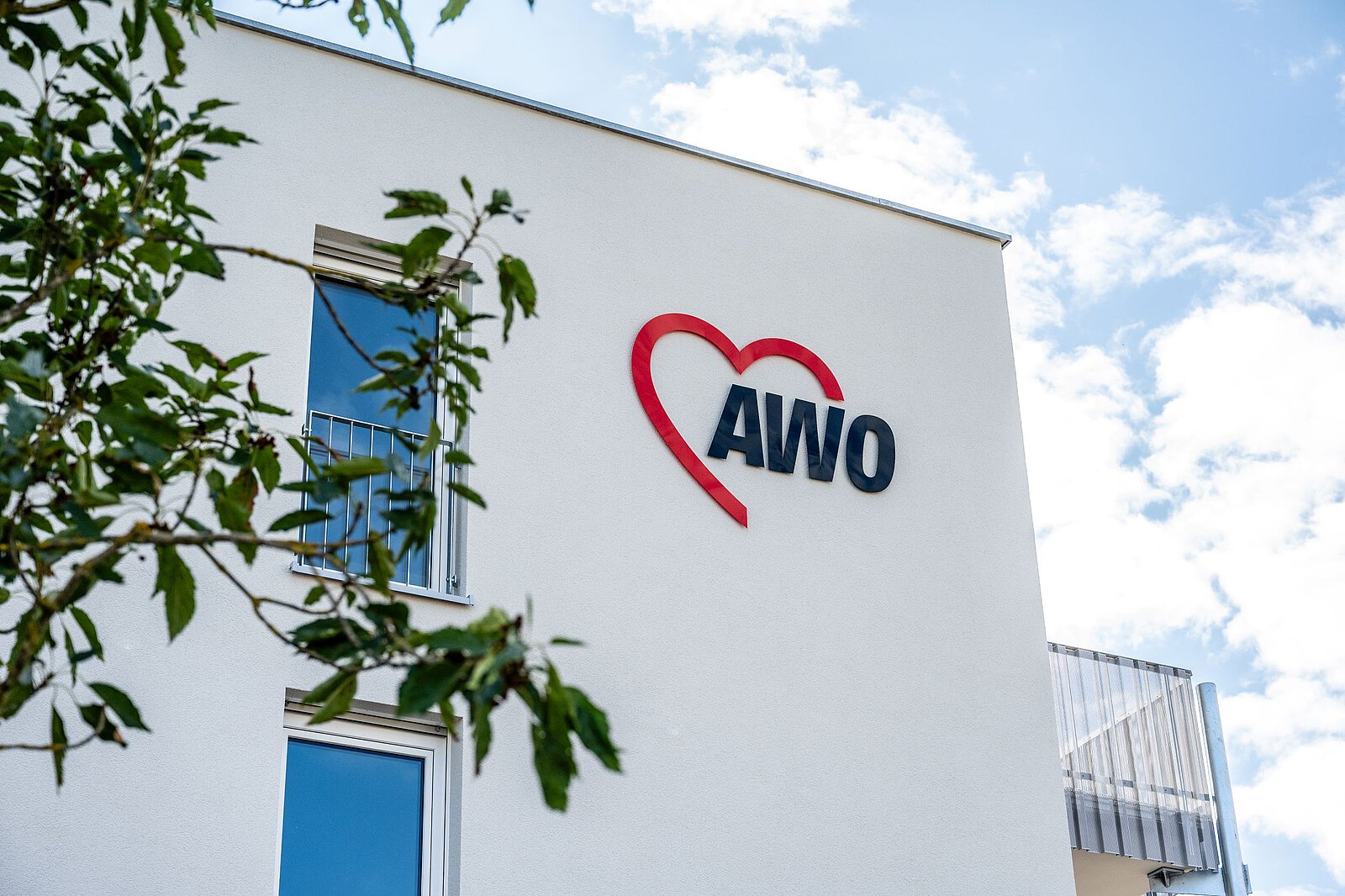 AWO-Logo auf weißem Putz, davor ein Baum