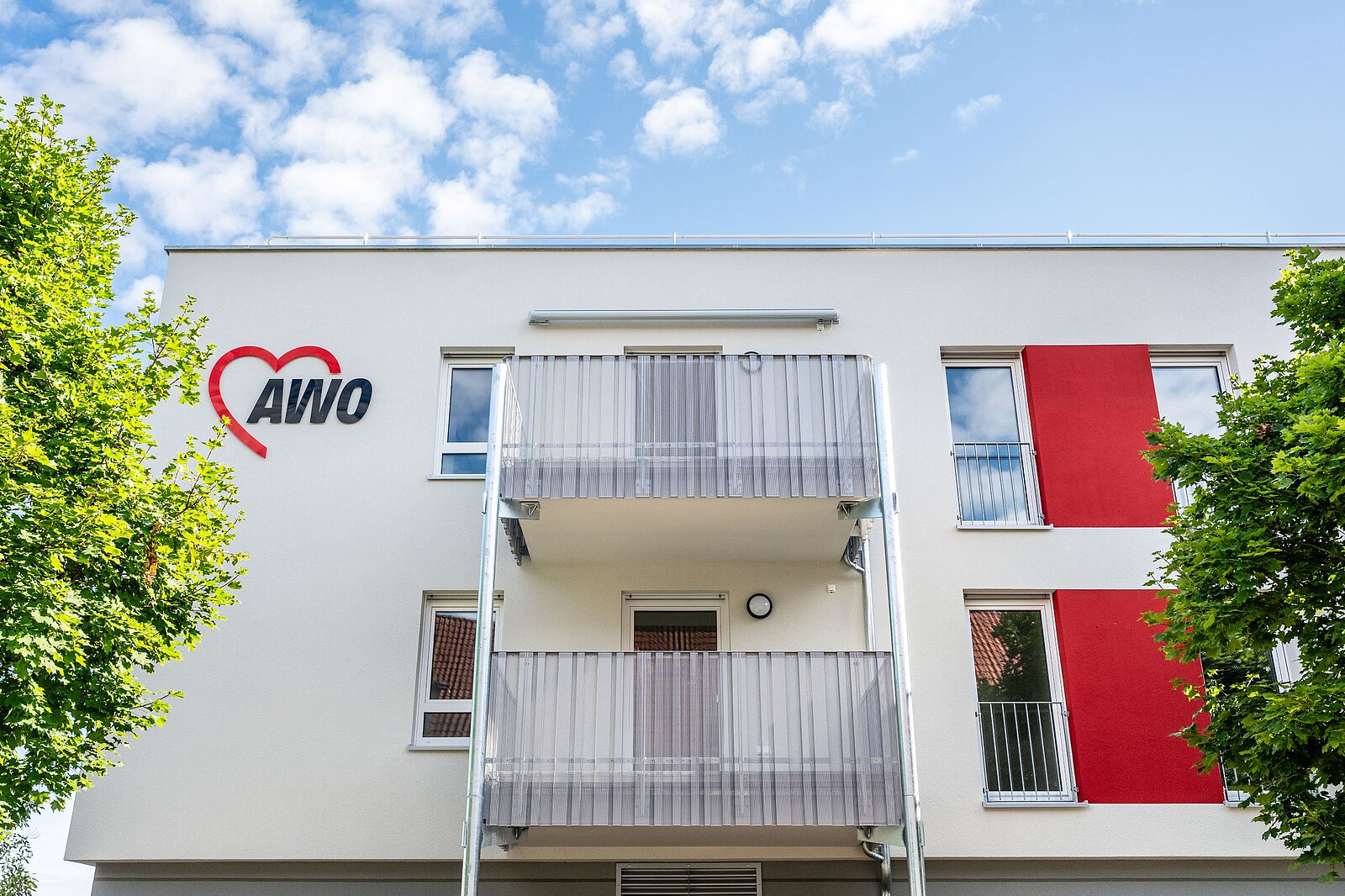Weiß-rote Fassade mit AWO-Logo und Balkonen, davor Bäume